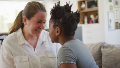 feliz mujer caucásica y su hija afroamericana sonriendo en la sala de estar