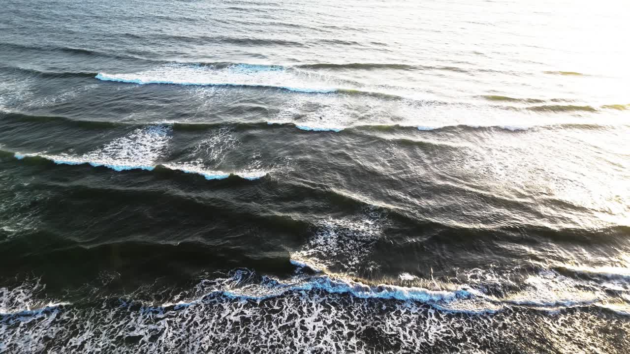 Lone Surfer Paddling Through Ocean Waves On West Coast Of Oregon In USA. aerial shot