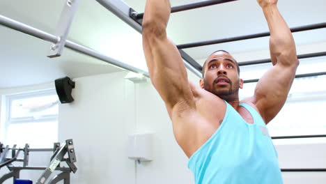 muscular young man exercising on monkey bars at a gym