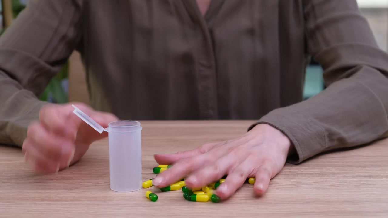 Woman empties small tablets from medicine container onto table