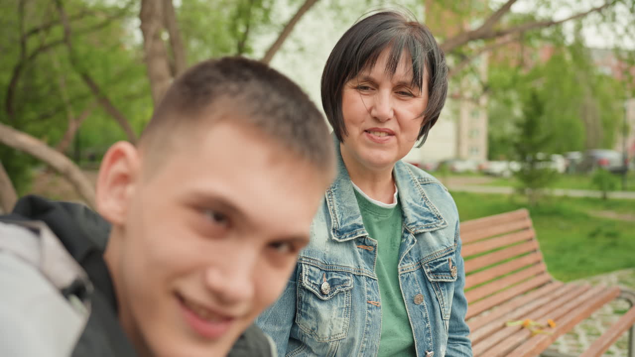 Woman Caregiver Addressing Young Man In Wheelchair With Firm Gesture On Bench In Park, Concerned Corrective Tone, Expressive Faces, Open Palm Communication, Leafy Background, Tension Mixed With Care