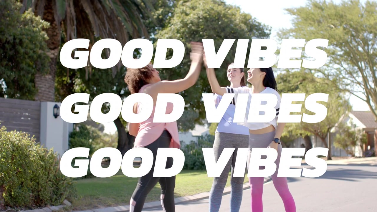 Drei Frauen beenden Training im Fitnessstudio, sehen Telefon mit aufleuchtendem 'GOOD VIBES' über einer Gruppe sich abklatschender Frauen.