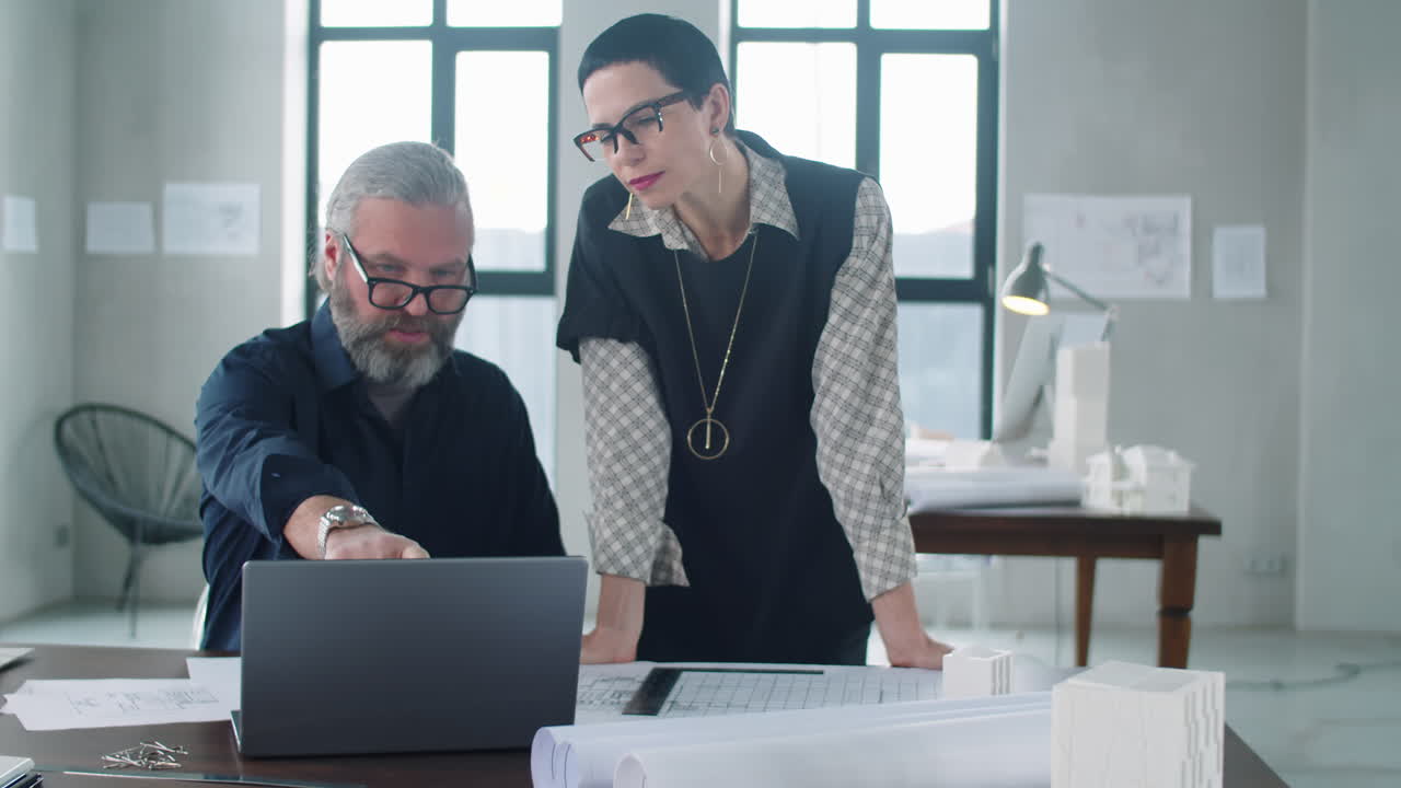 dos colegas discutiendo un proyecto en una computadora portátil en una oficina de arquitectura