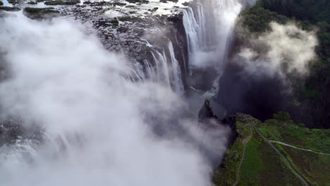 Aerial view of Victoria Falls with powerful waterfall plunging into gorge, mist rising above lush green forest, dramatic natural wonder and iconic travel destination in Africa