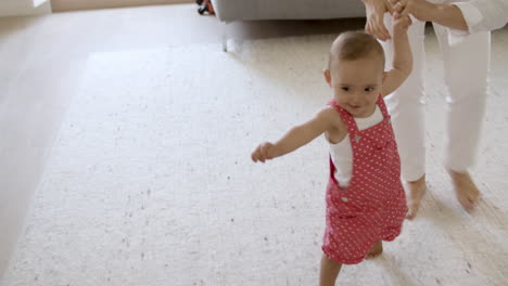 Happy baby girl taking her first steps with difficulty in living room