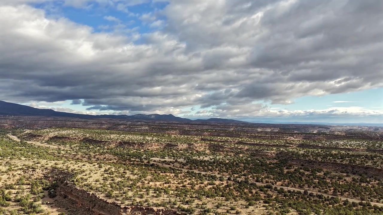 Un hyperlapse cinematografico realizzato con drone cattura mesas drammatiche e sagome di nuvole su un epico paesaggio del sud-ovest. Le auto che percorrono l'autostrada sottostante aggiungono un senso di scala e movimento a questa vasta veduta.