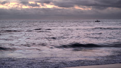 a small boat makes its way south on the pacific ocean under a cloudy somber sky