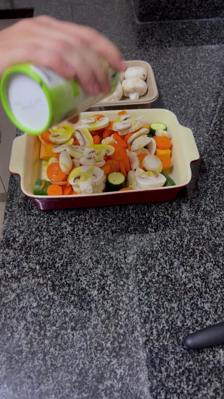 A man's hand is visibly pouring salt over vegetables that are to be roasted. The vegetables are mushrooms, carrots, butternut and baby marrow