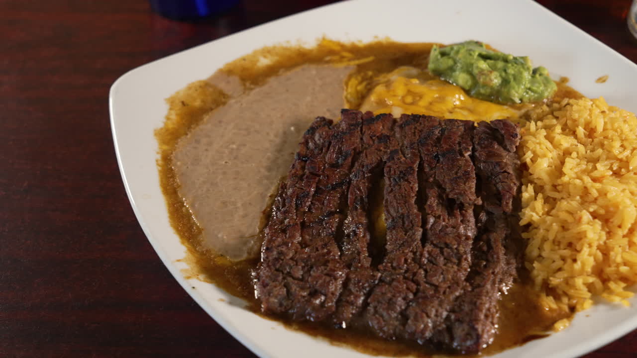 enchiladas tradicionales de queso tampiquena con carne asada a la parrilla en la parte superior combinadas con frijoles refritos y arroz mexicano, deslizador de cerca 4k