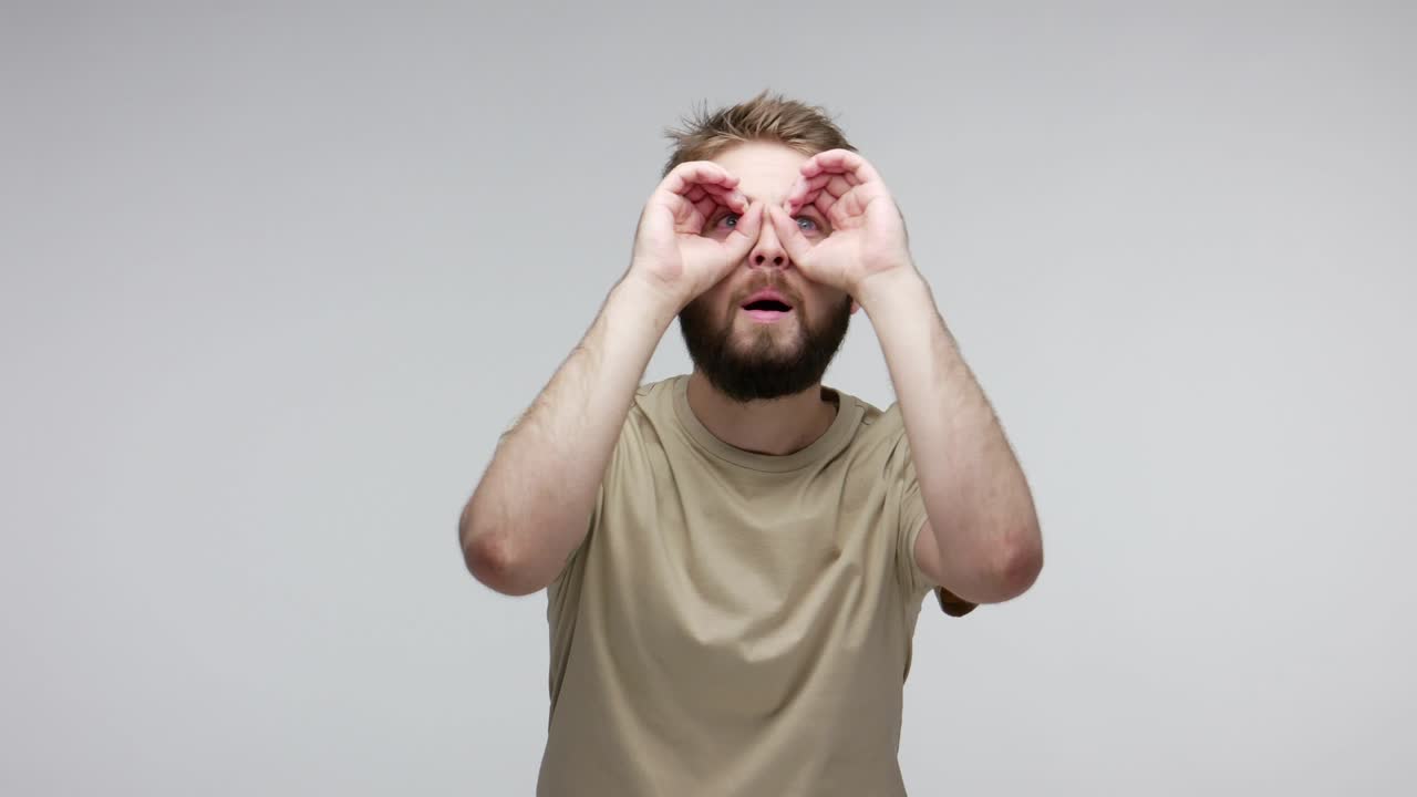 un tipo curioso observando el lejano horizonte, mirando a través de los binoculares, gestos de la mano, expresando asombro.