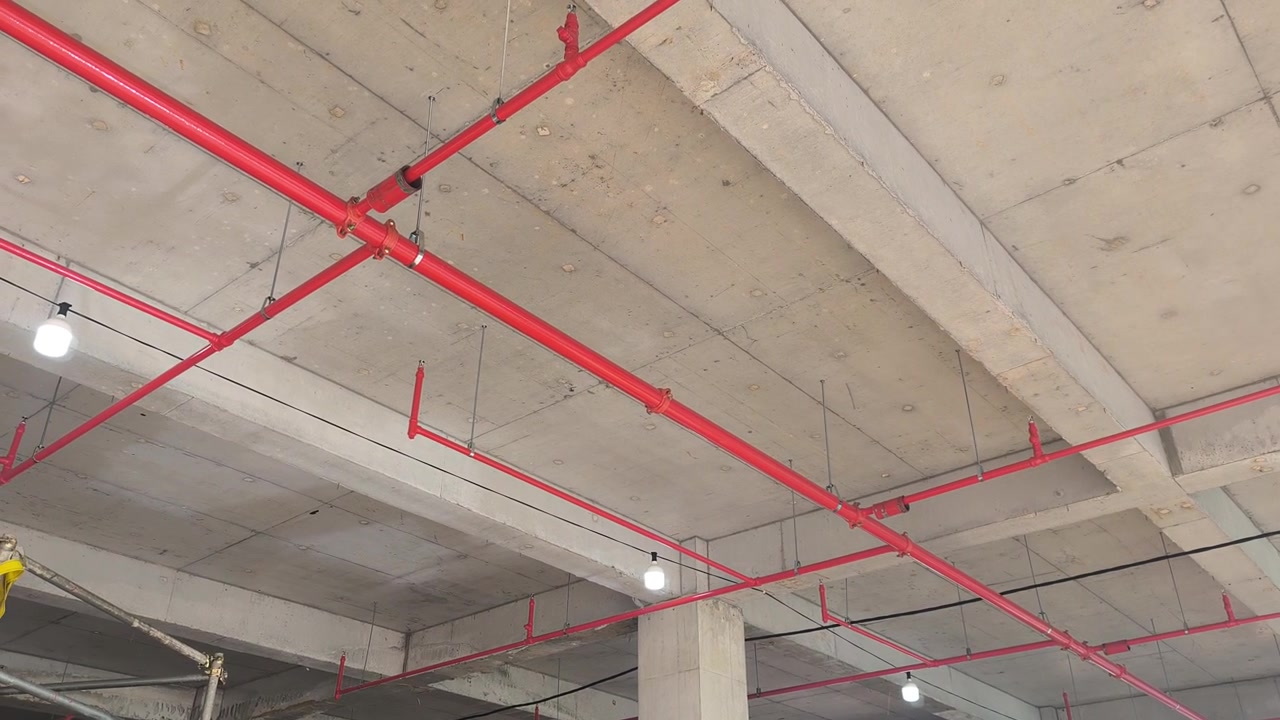 Operai installano una rete di tubazioni antincendio sprinkler in un cantiere edile. Realizzato secondo precisi progetti ingegneristici, questo sistema vitale eroga acqua per sopprimere gli incendi iniziali prima dell'arrivo dei vigili del fuoco