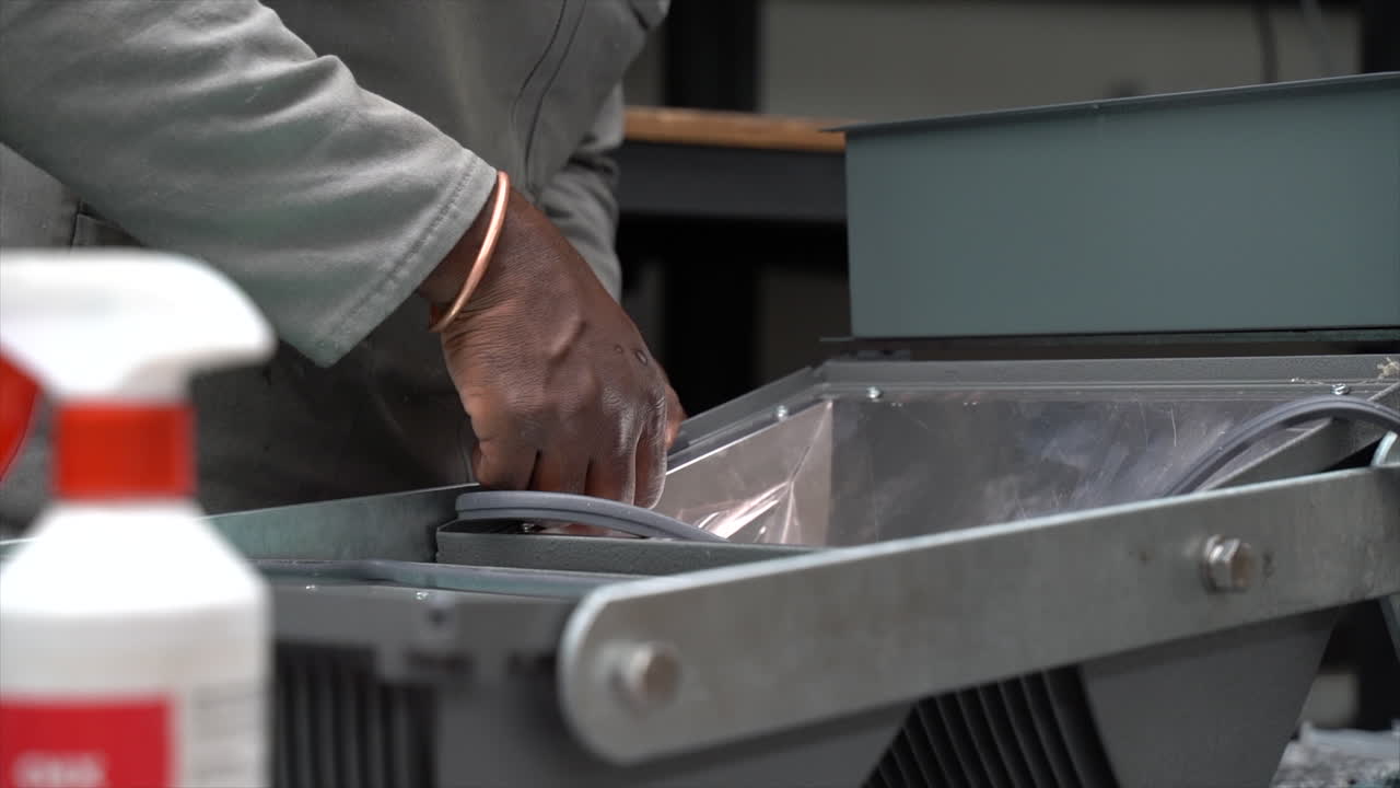 Black production line worker assembling LED light in a factory