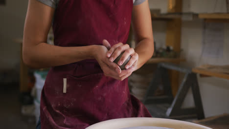 Mid-section-of-female-potter-keeping-a-ball-of-clay-on-potters-wheel-at-pottery-studio