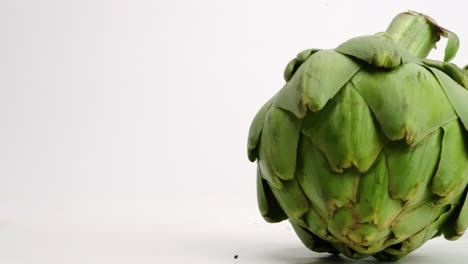 fresh green whole artichokes falling onto white table top and rolling around in slow motion