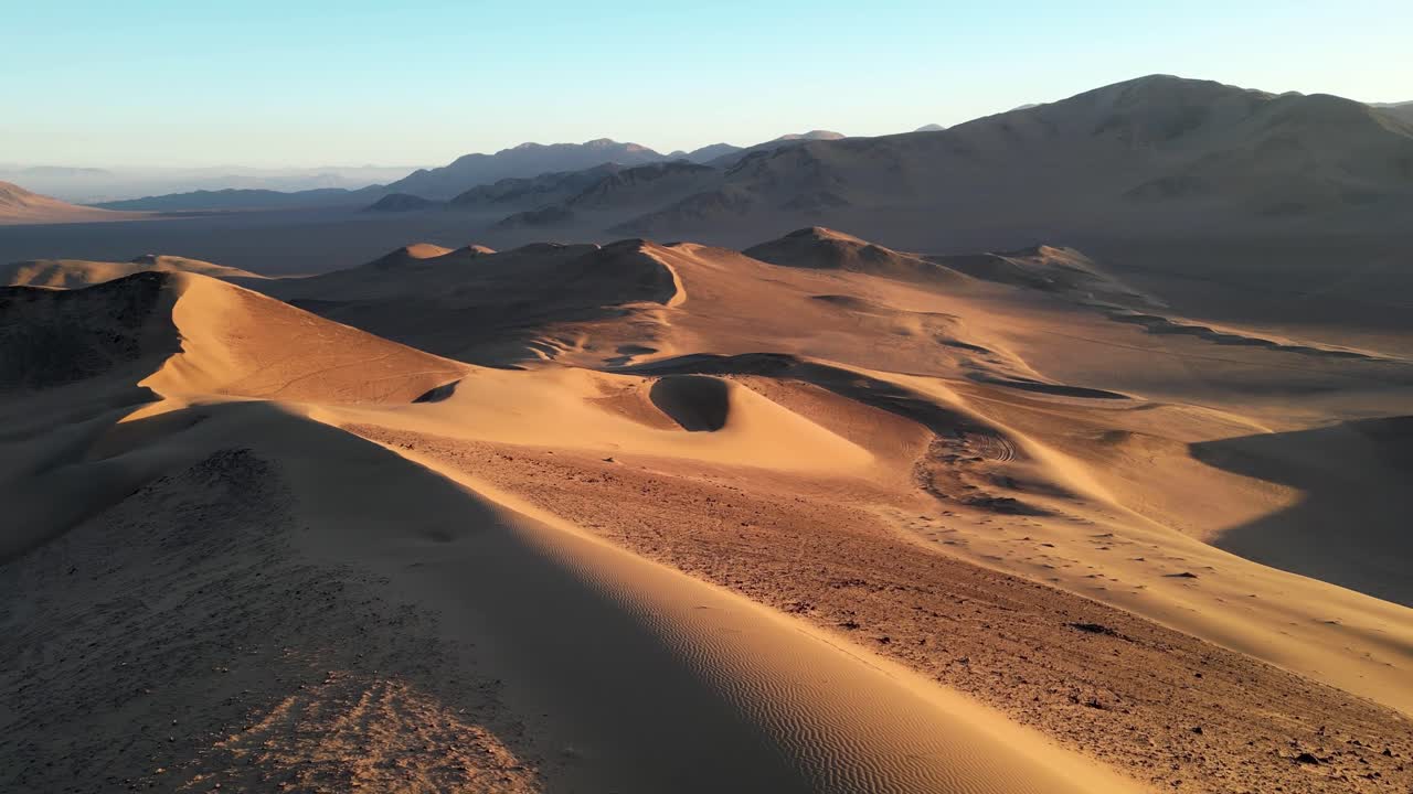 Sorvolo di un drone su un terreno desertico spoglio nell'entroterra del Cile, immerso nei tenui colori del tramonto con lunghe ombre