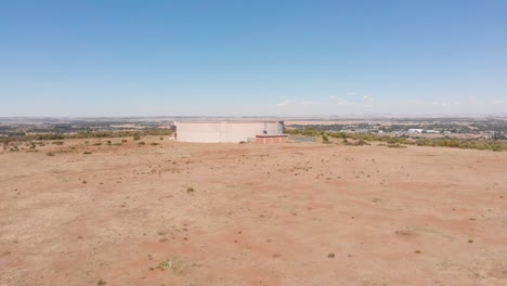 DRONE-Reveal-Shot-of-Water-Supply-Tank-supplying-water-to-a-Town-in-the-Background-on-a-Sunny-Day