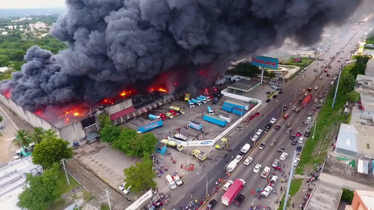 Aerial view of a building fire, dark smoke rising from a warehouse in flames, bright day, Vandalism in Mexico city - tilt up, drone shot