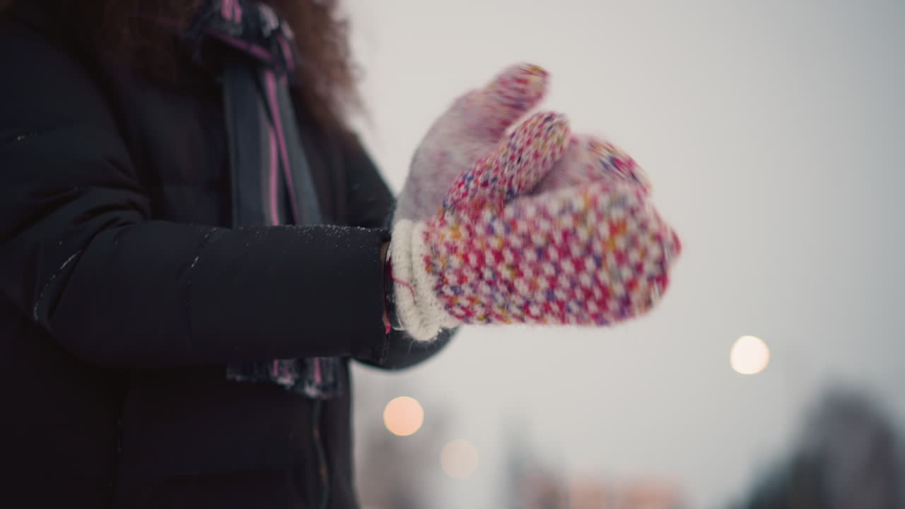 Skater wearing colorful knitted mittens claps hands outdoors during cold winter day, snowflakes scattering from wool texture, creating cozy seasonal scene with warmth, movement and festive winter atmosphere