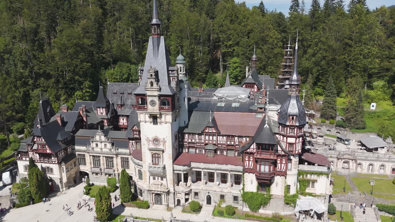 Drone orbiting around Peles Castle, showing its roofs, towers, and forested surroundings