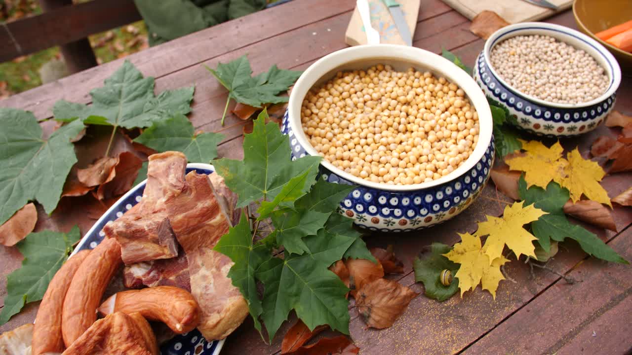 야외 피크닉에서 소시지, 베이컨, 야채, 감자, 당근, 완두콩, 조미료로 가득 찬 식사 테이블을 닫습니다.