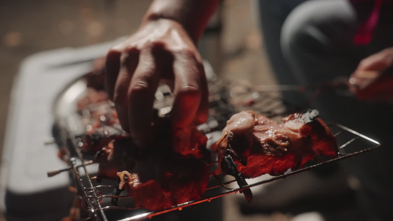 Memasak di atas api. Peserta kemping menyiapkan makan malam di dekat panggangan panas. Potret dekat daging mendesis di atas arang yang membara. Koki kemping yang aktif dengan hati-hati memanggang ayam dengan cahaya berasap dan nyala api yang hidup