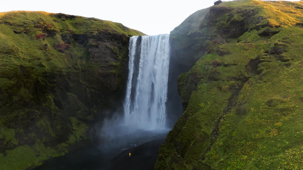hombre con chaqueta amarilla cerca de la cascada de skogafoss en islandia - disparo de avión no tripulado