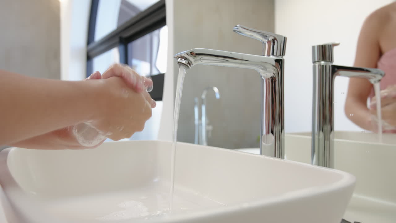 Washing hands with soap under running water in modern bathroom sink