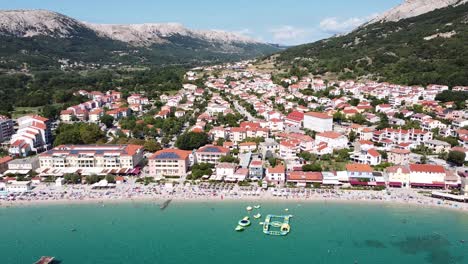 Playa-De-Baska,-Isla-De-Krk,-Croacia---Vista-Aérea-De-Drones-Del-Balneario-Con-Costa,-Turistas,-Bulevar,-Tumbonas-Y-Parque-Acuático