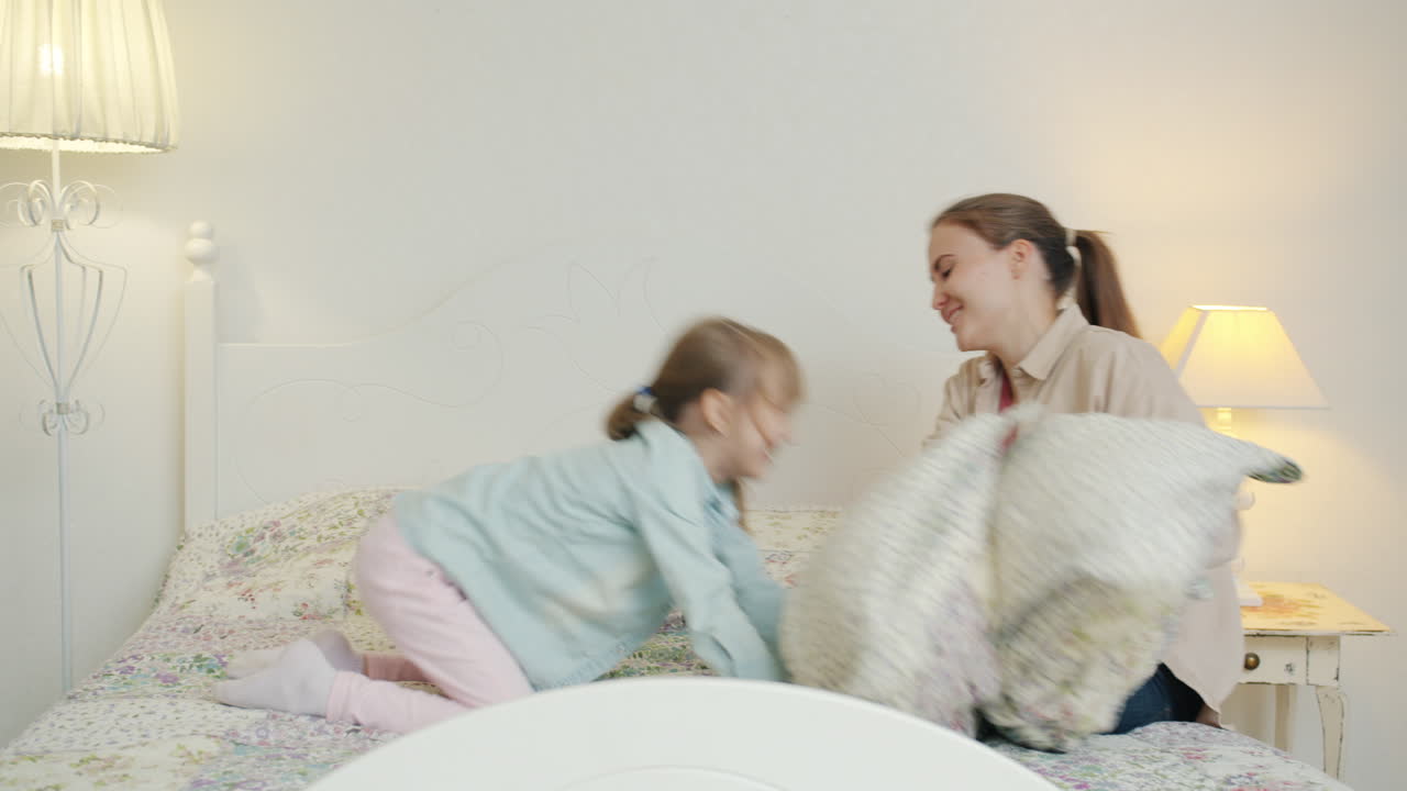 Madre e figlia che fanno una battaglia di cuscini in camera da letto
