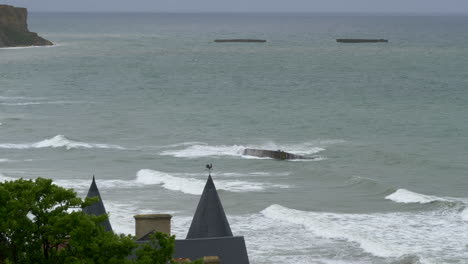 Waves-of-turbulent-sea-flood-the-coast-of-Mulberry-Artificial-harbor,-Arromanches-les-Bains,-Normandy