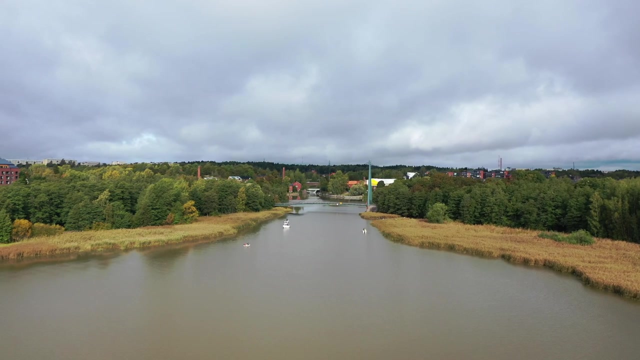 Bredt luftfoto af Helsinkis byskyline med Kalasatama-skyskrabere og Hanasaari kraftværk på tværs af Vanhankaupunginselkä-bugten. Naturskønt kystbylandskab under en stemningsfuld, skyet himmel.