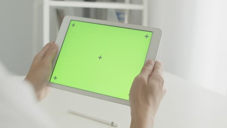 un hombre de negocios asiático sentado en una silla usando una tableta con pantalla verde en la sala de oficina, desplazándose por las redes sociales o viendo contenido en línea, concepto de comunicaciones.