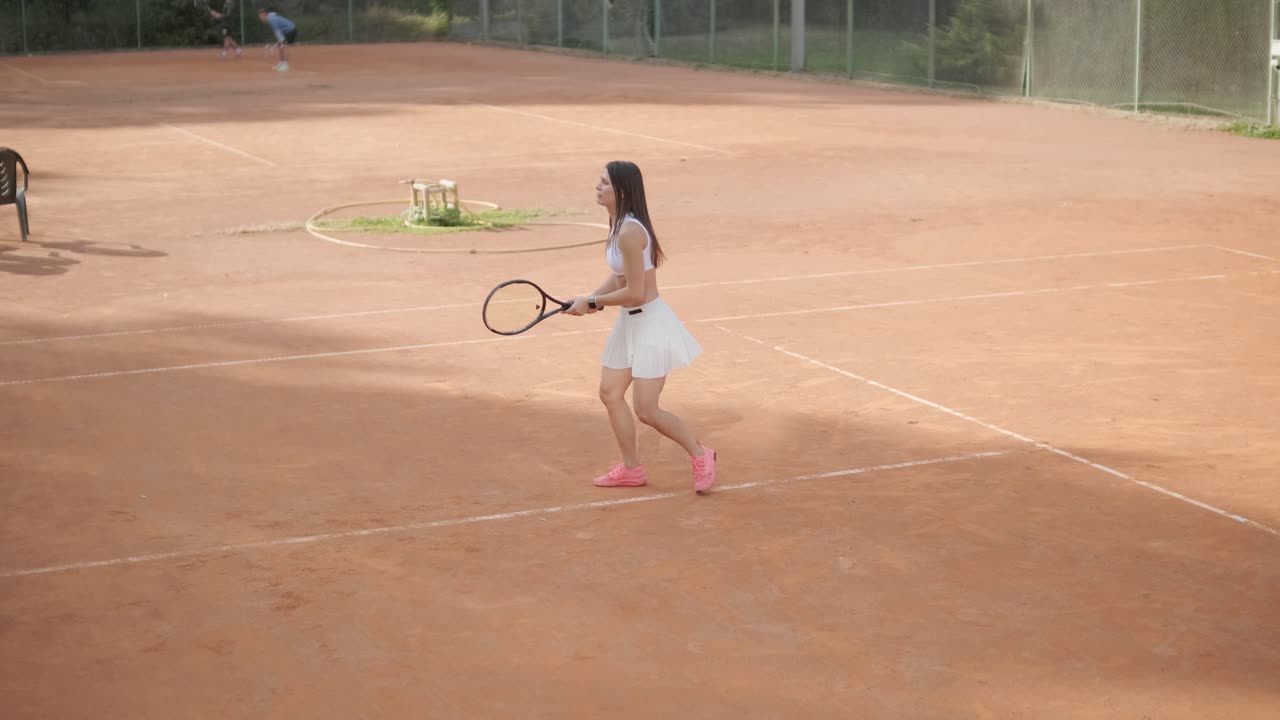 코치와 함께 야외 코트에서 테니스를 연습하는 젊은 여성. 코치는 선수가 그녀의 기술에 대해 일하면서, 운동 훈련 세션에서 그녀의 스트로크를 완성하는 동안 지침을 제공합니다.