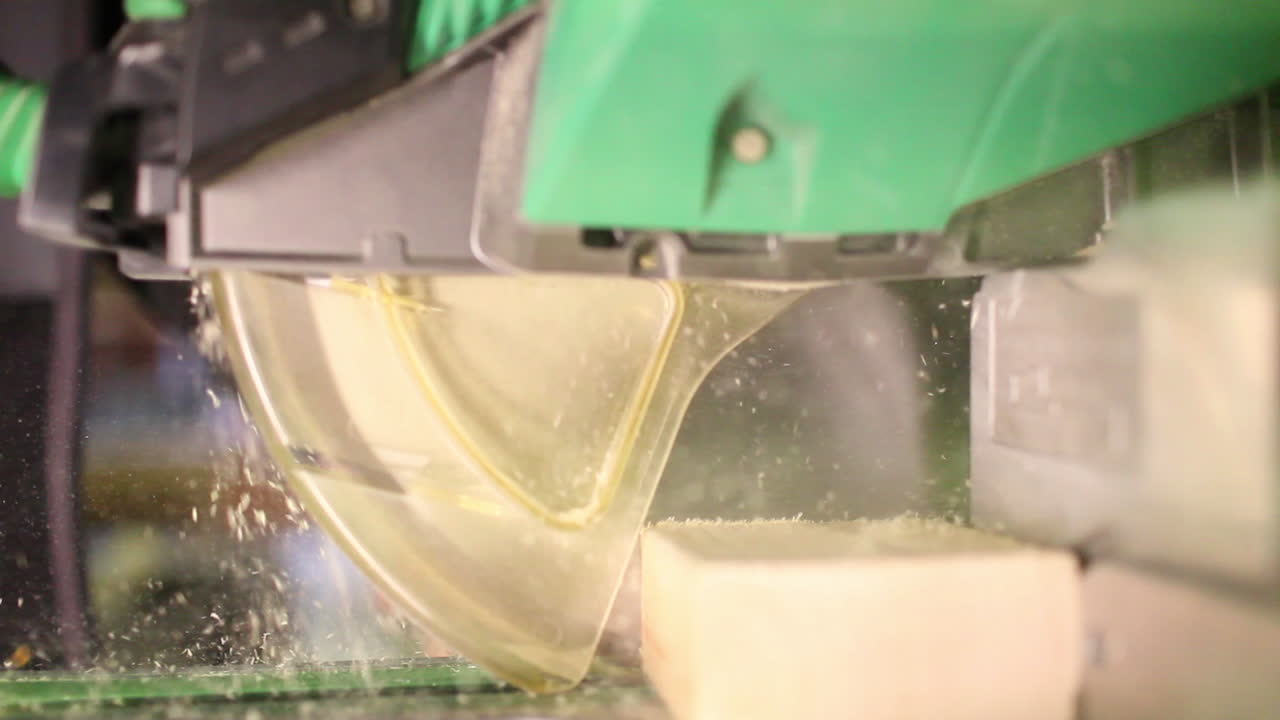 An extreme close-up of a person using a miter saw to cut an oak board