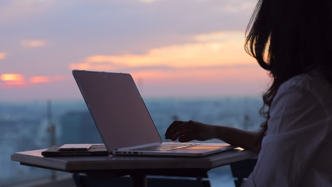 Cropped view of Woman typing on keyboard while sitting at her working place in cozy, relaxing in summer beautiful sunset sky.
