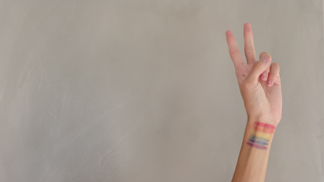 Hand with rainbow flag tattoo making peace sign, symbolizing LGBTQ+ pride