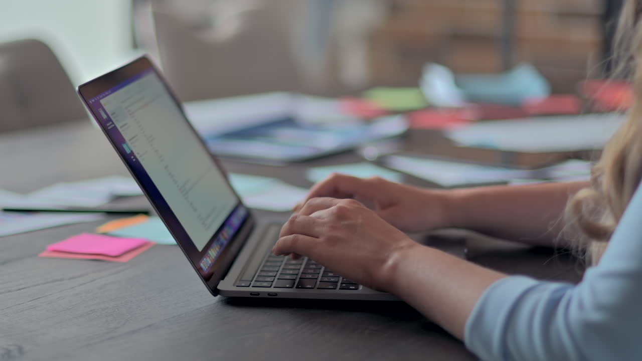 Kvinde der skriver på en bærbar computer ved et skrivebord på et kontor