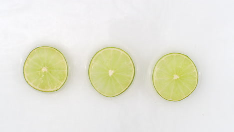 splashes of water fall on sliced lime green rings on a white background. super slow motion.