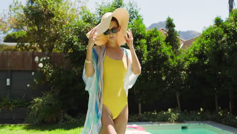 woman in yellow swimsuit walking confidently by pool, wearing sunglasses