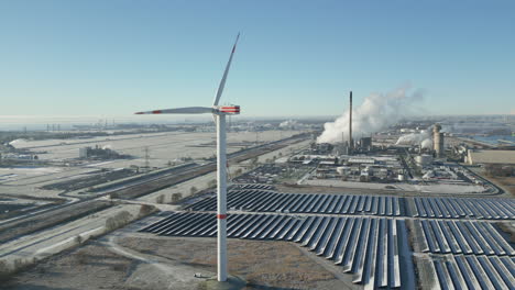 turbina eólica girando en un paisaje helado, planta industrial humeante, paneles solares, toma aérea de drones