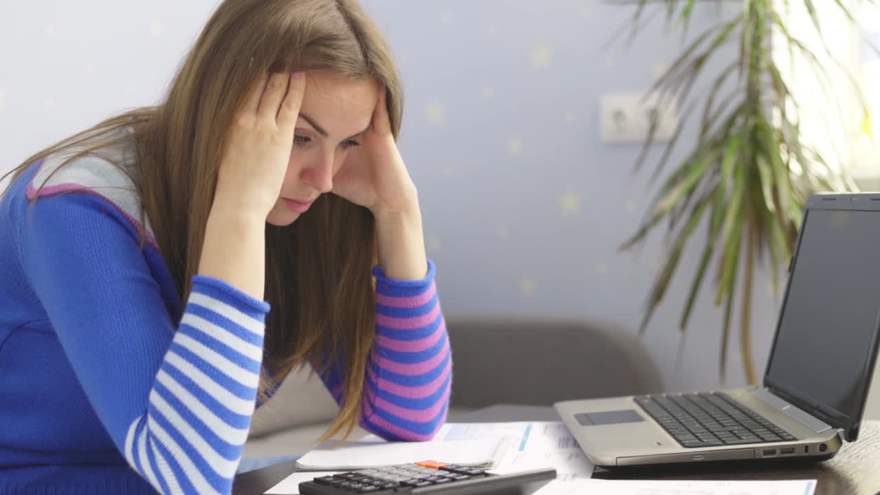 Stressed young brunet woman sits at home manage household finances frustrated with family financial problems. Distressed upset female disappointed with money debt, pays bills taxes online on laptop