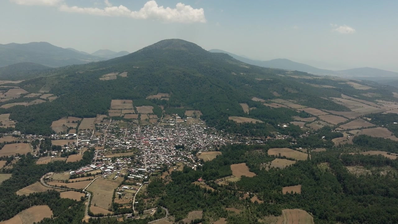 Uma imagem de drone em ângulo elevado revela a cidade rural de Chavinda, cercada por campos verdes e picos.