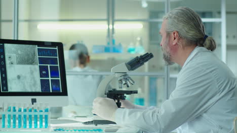senior scientist working with microscope and computer in lab