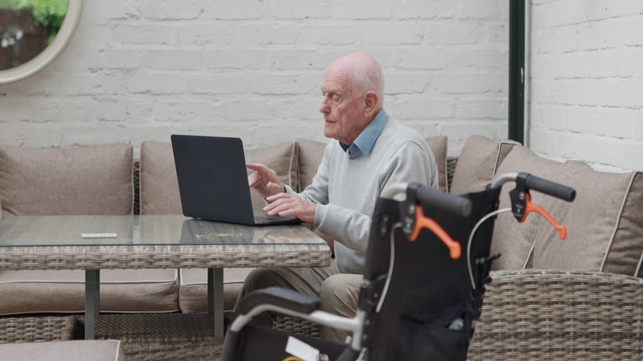 Uomo anziano che usa un laptop con una sedia a rotelle nelle vicinanze