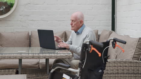 Senior man using laptop with wheelchair nearby