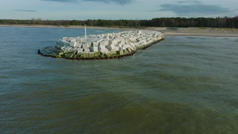 aerial establishing view of protective stone pier with concrete blocks and rocks at baltic sea coastline at liepaja, latvia, strengthening beach against coastal erosion, drone shot moving forward low