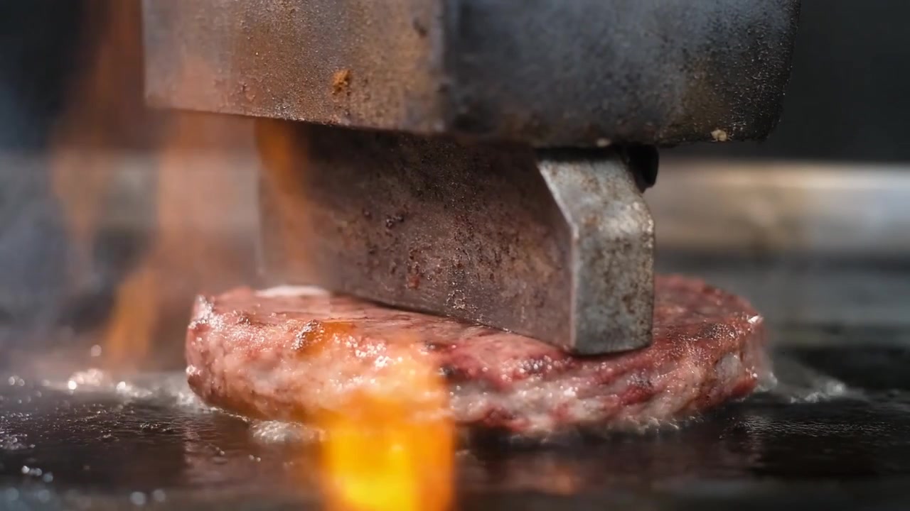 Oksekødsburgerbøf syder og presses på en varm grill