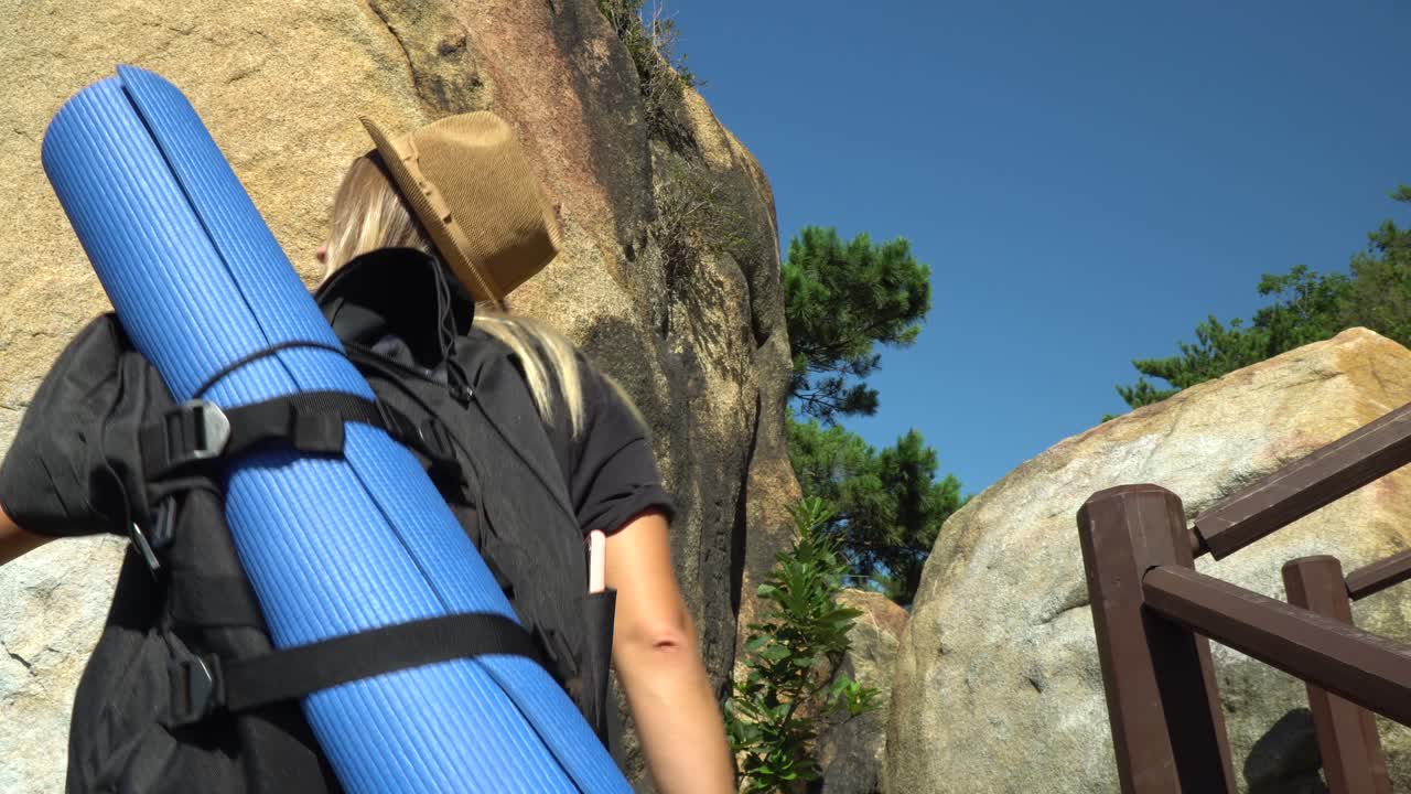 배낭에 요가 매트와 함께 계단을 오르는 백인 금발 소녀