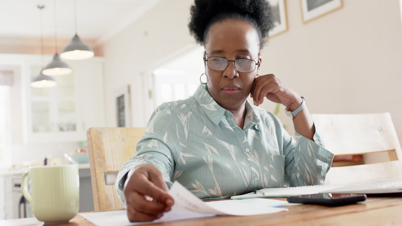 Felice donna anziana afroamericana che sbriga pratiche e usa il laptop in una stanza soleggiata, al rallentatore