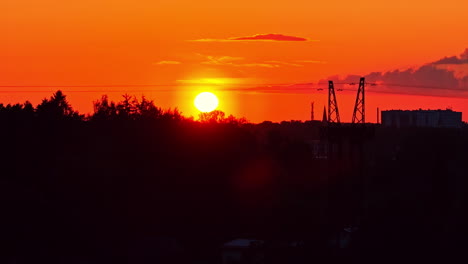 silhouette of a large power line pylon against a stunning, fiery orange sunset over a forested landscape in latvia, blending nature and industry - an aerial drone shot